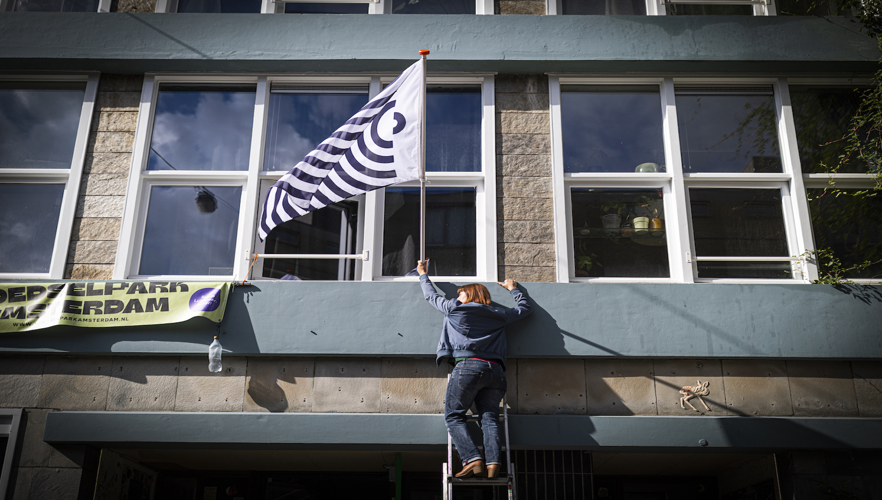persoon plaatst vlag aan gevel van ouder gebouw